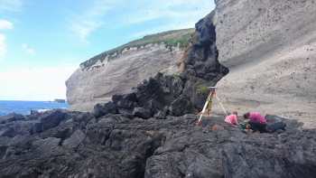 GeoNet technicians working on GNSS reference point in the lee of Macauley Island's volcanic cliffs. 